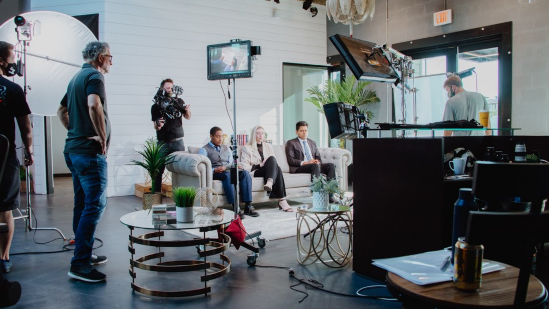 Actors sit on a couch as director oversees video shoot