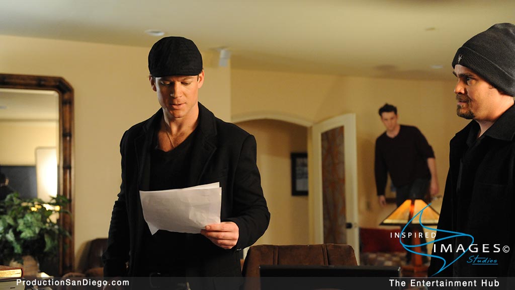 A man dressed in black reads paper while two other men watch