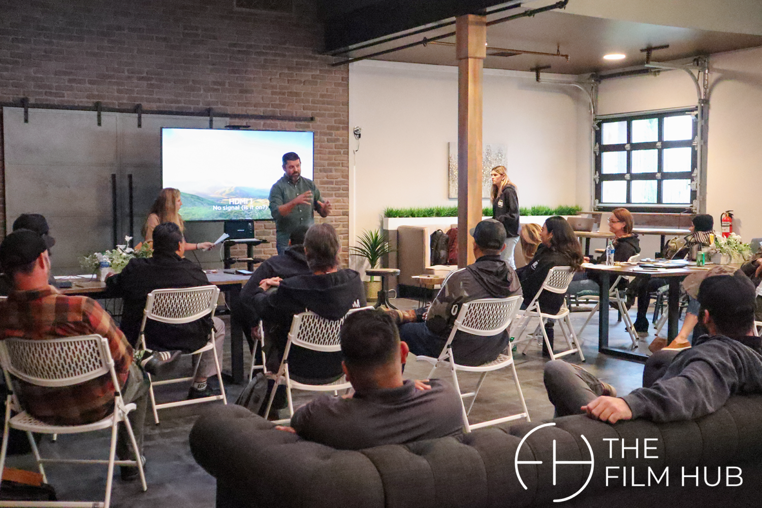 a group of people are seated, listening attentively to a speaker going over a powerpoint at The Film Hub