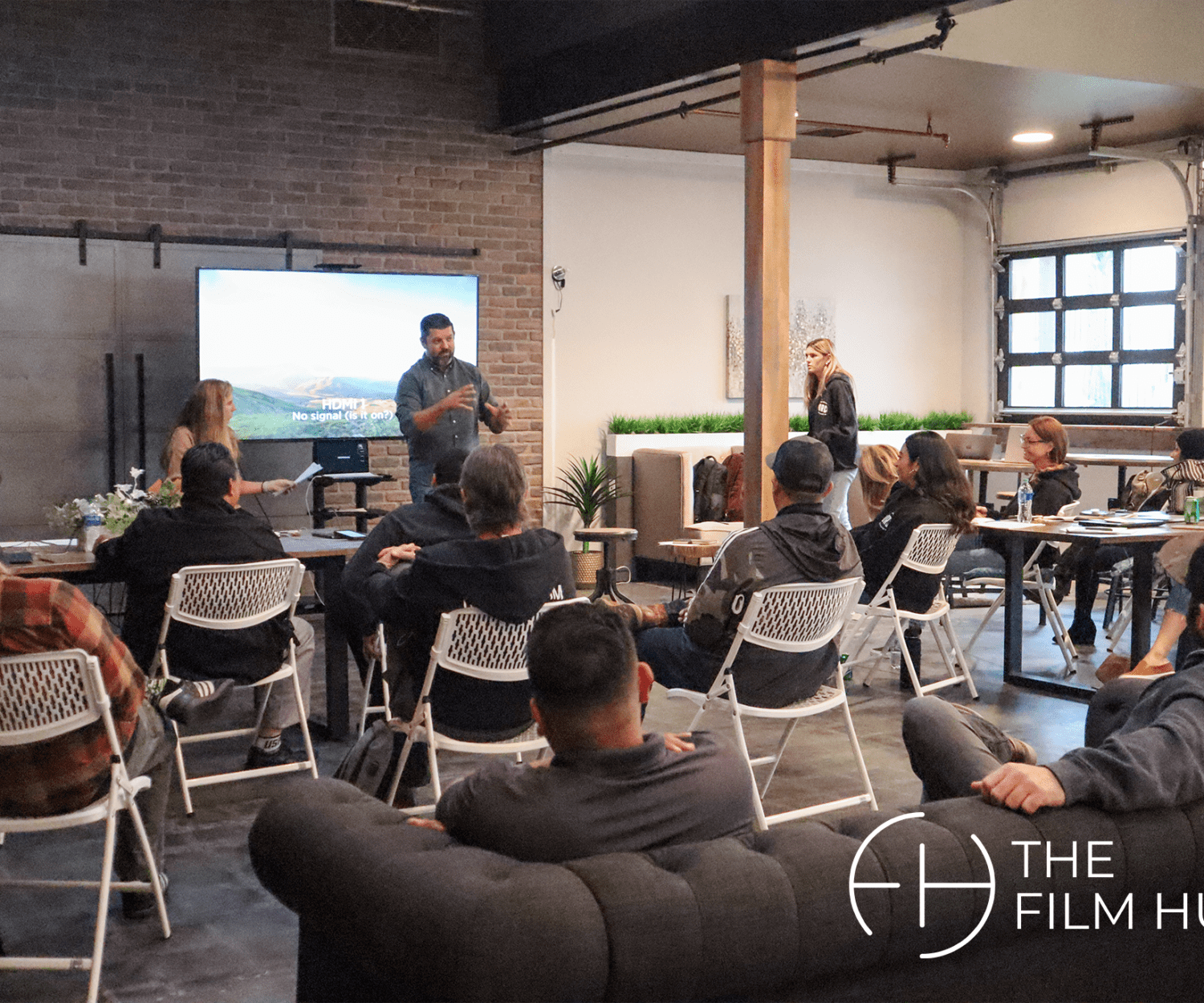 a group of people are seated, listening attentively to a speaker going over a powerpoint at The Film Hub
