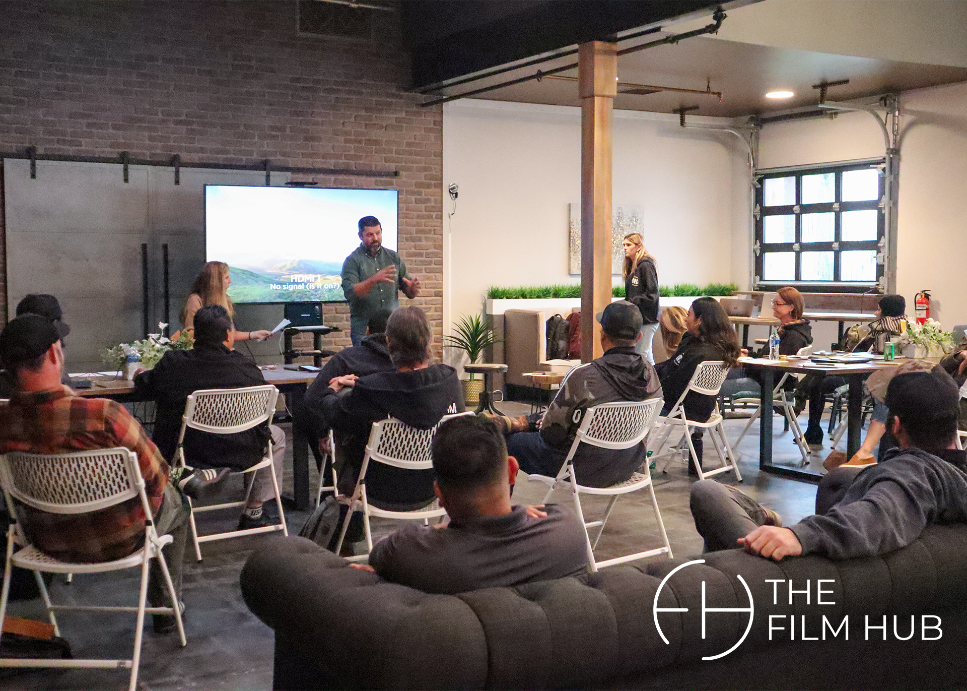 a group of people are seated, listening attentively to a speaker going over a powerpoint at The Film Hub