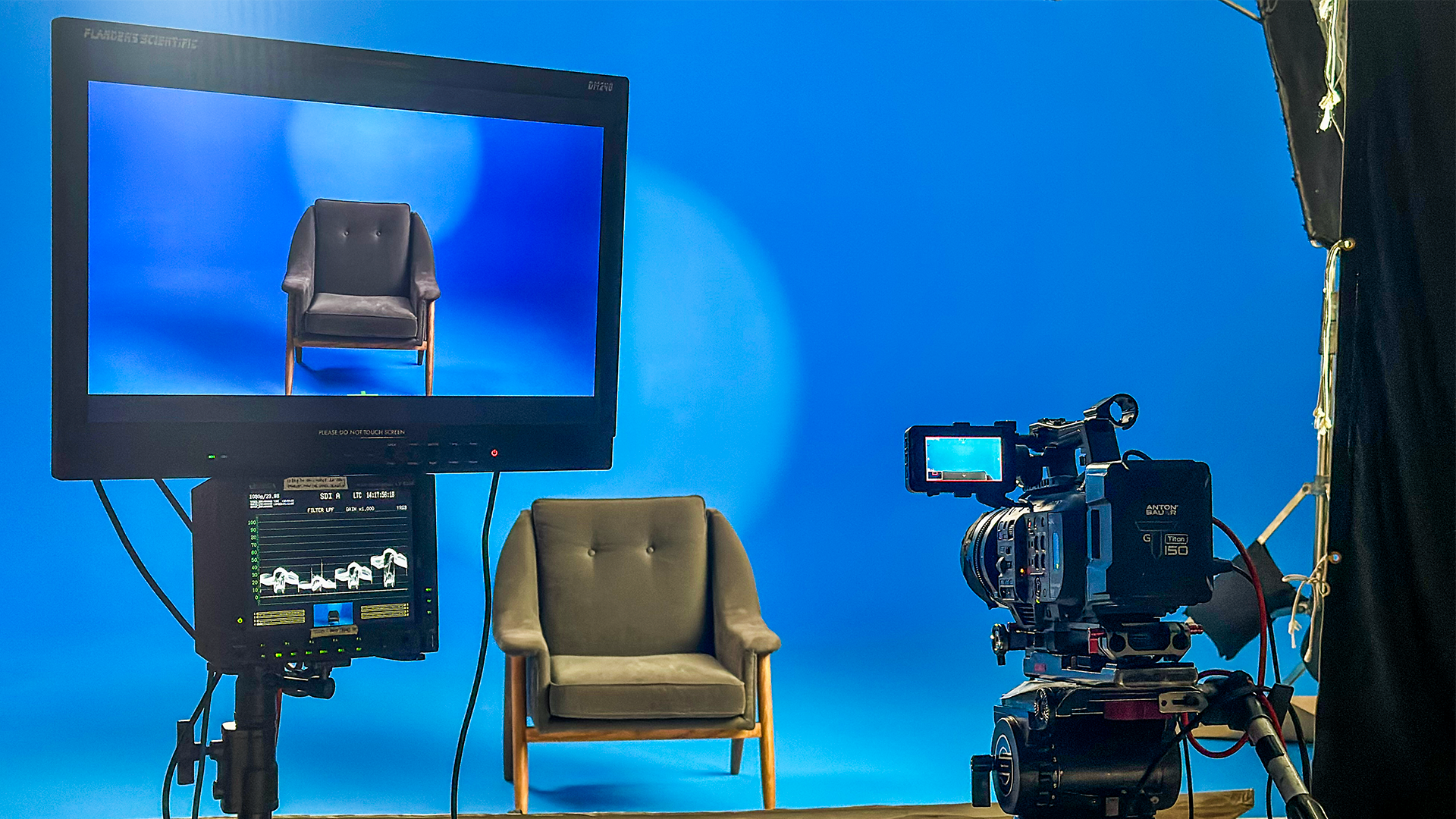 Professional video production setup featuring a camera and monitor focused on a single chair in front of a seamless blue backdrop, inside The Film Hub stage 2