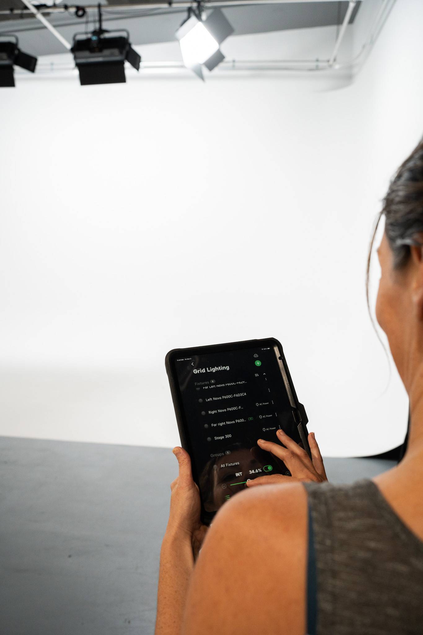 Close-up of a person using a tablet to control ceiling-mounted Aputure Nova P600c RGB LED lights in Stage 2 at The Film Hub, with a white cyclorama in the background.