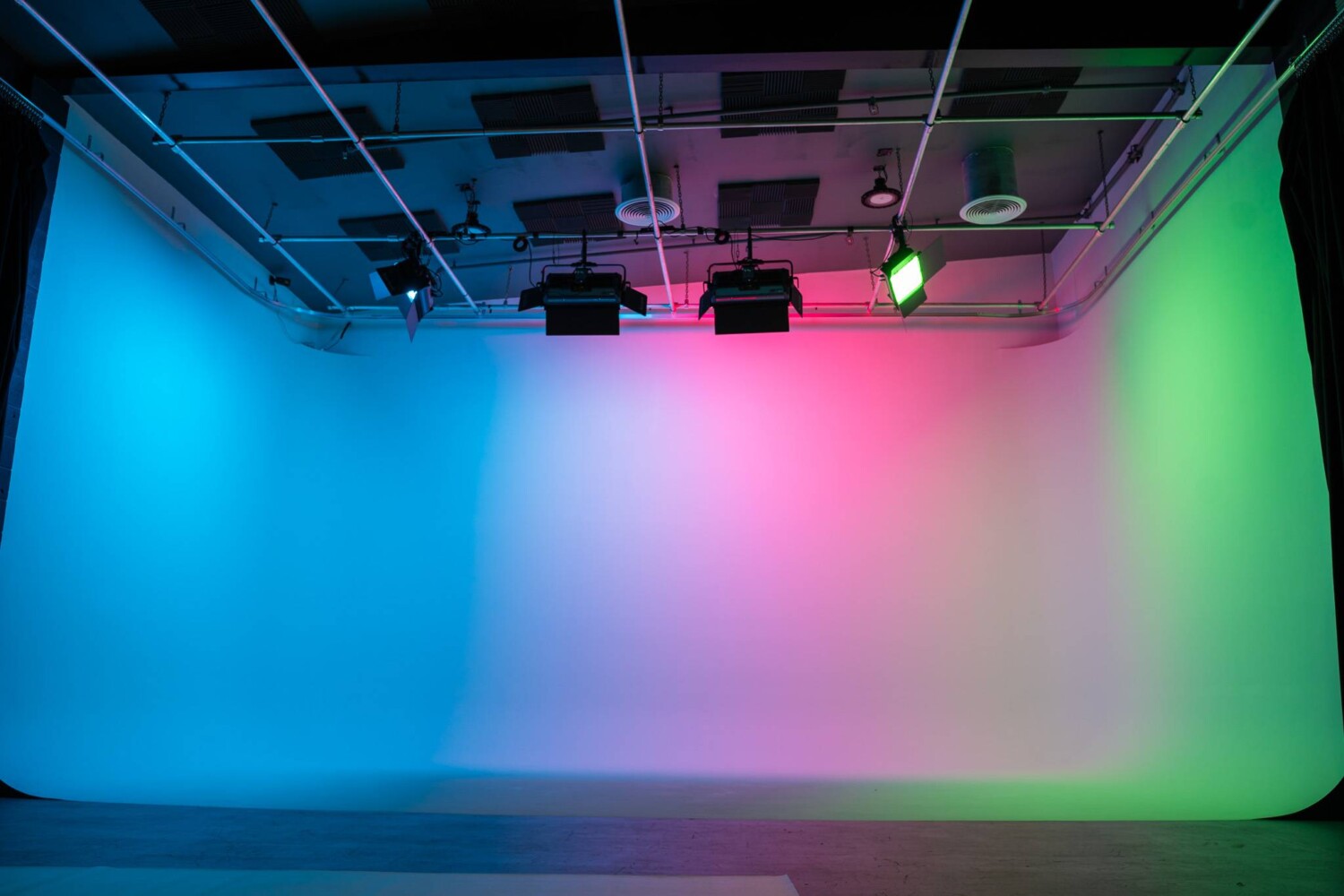 Pre-lit three-wall white cyclorama at The Film Hub’s Stage 2, illuminated with ceiling-mounted Aputure Nova P600c RGB LED lights displaying vibrant blue, pink, and green hues.