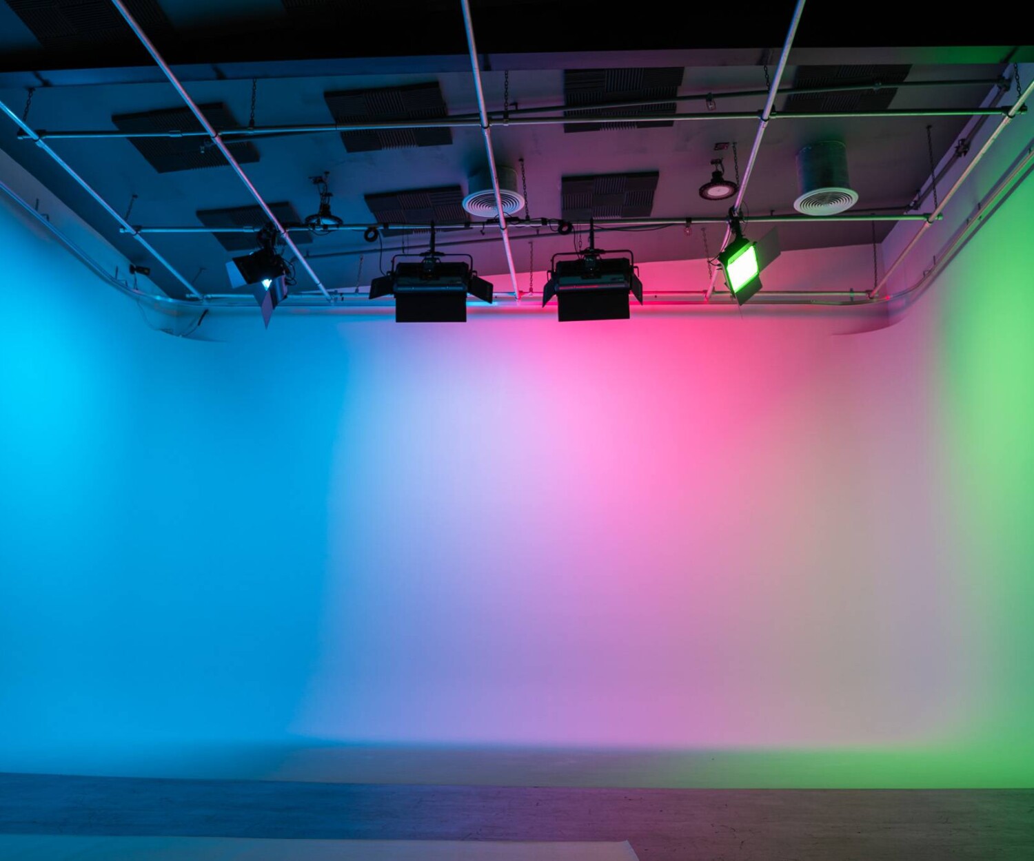 Pre-lit three-wall white cyclorama at The Film Hub’s Stage 2, illuminated with ceiling-mounted Aputure Nova P600c RGB LED lights displaying vibrant blue, pink, and green hues.