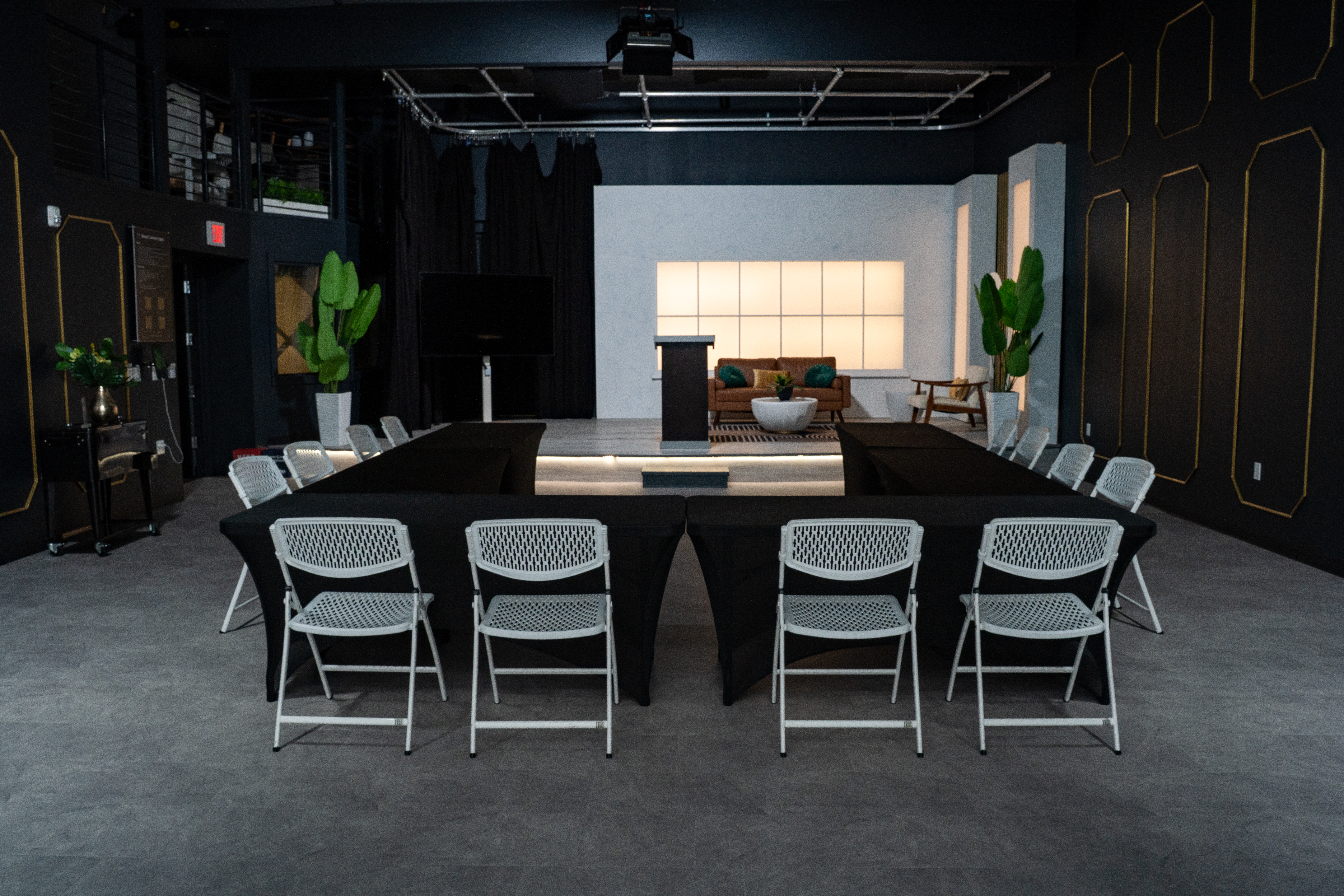 U-shaped table and chair setup at Stage 2 in The Film Hub, with a podium, LED-lit backdrop, lounge seating area, and modern black-and-gold Art Deco interior design.