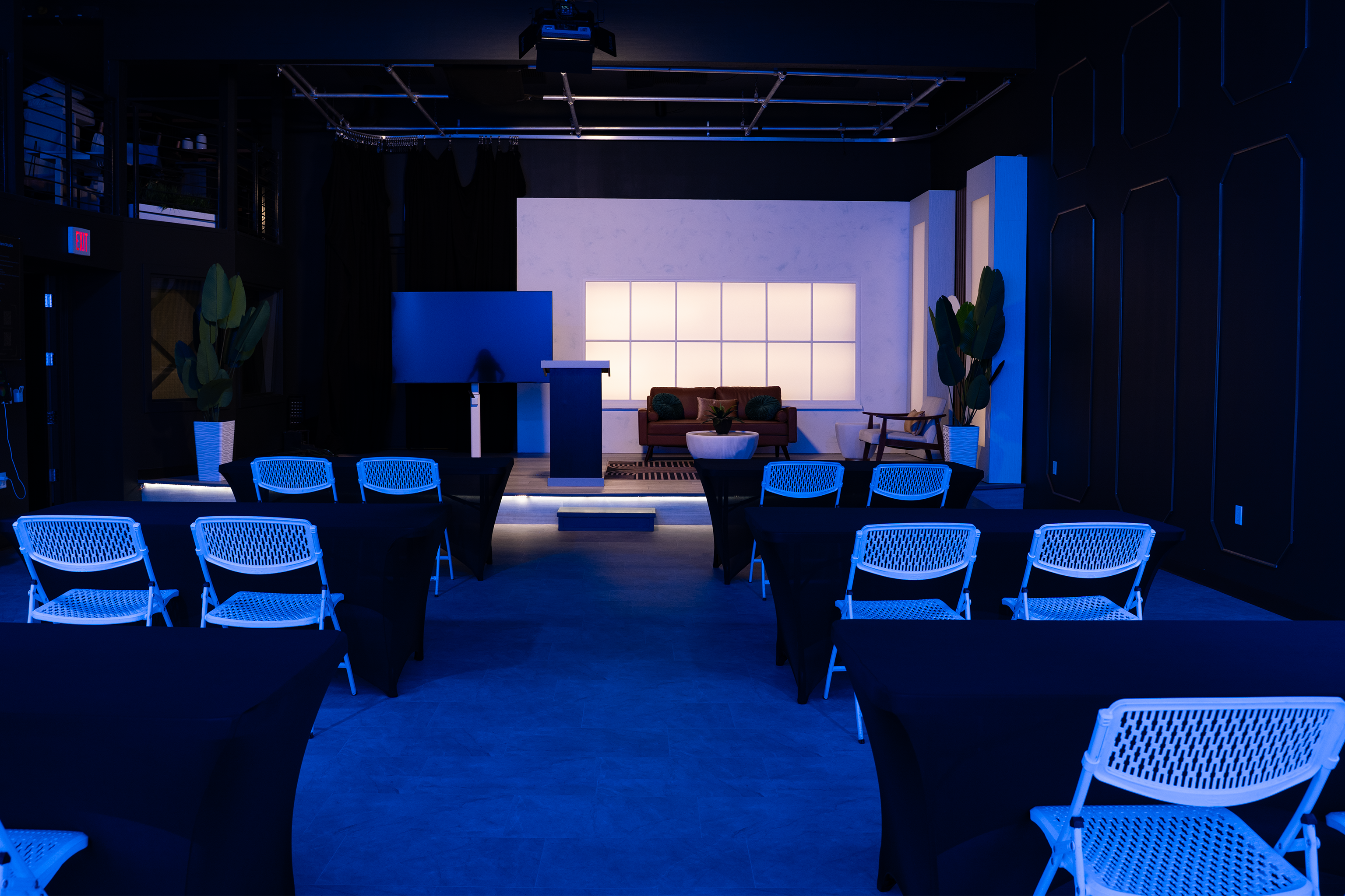 Event setup at The Film Hub’s Stage 2 featuring blue RGB lighting, rows of white chairs and black-covered tables, LED-lit backdrop, podium, and modern lounge area on raised platform.