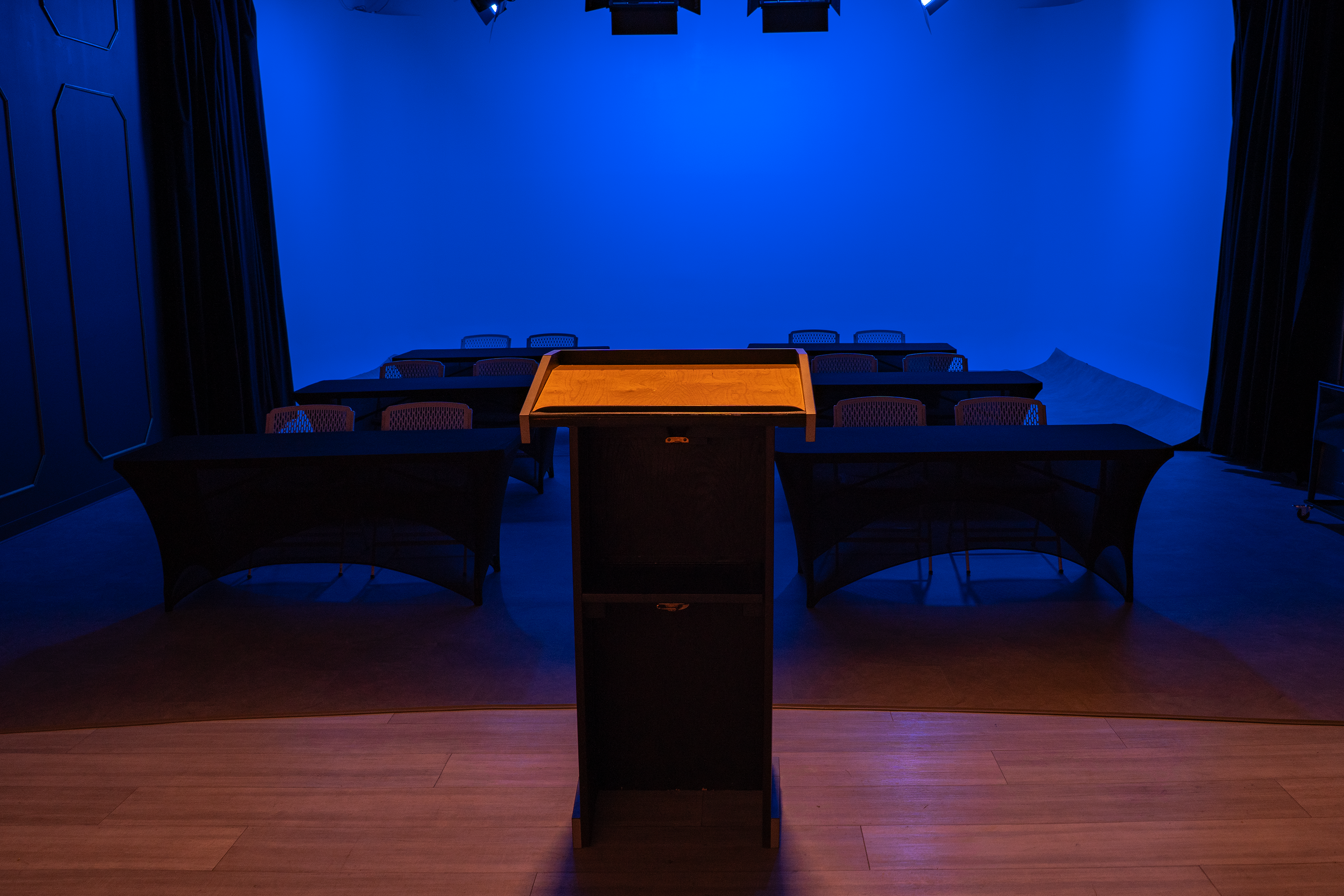 View from podium in Stage 2 at The Film Hub with rows of tables and chairs under vibrant blue lighting, ideal for presentations, panels, and speaker events.