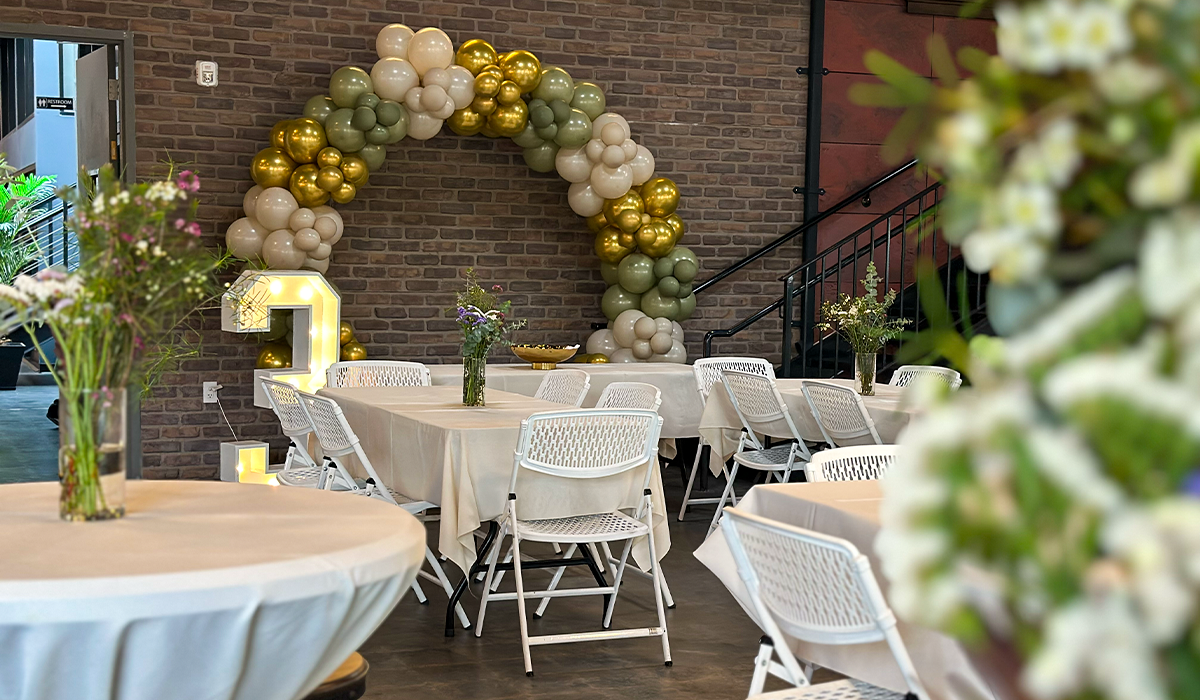 Close-up of balloon arch and floral centerpieces at an event in Audrey Hepburn Hall at The Film Hub, showcasing gold and green balloon decor and intimate round table arrangements.