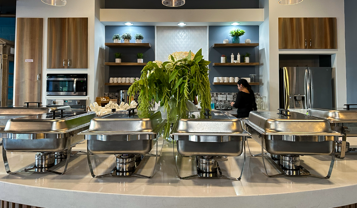 Catering setup with buffet warmers and floral centerpiece in the full kitchen of Audrey Hepburn Hall at The Film Hub, with event staff member preparing behind the counter.